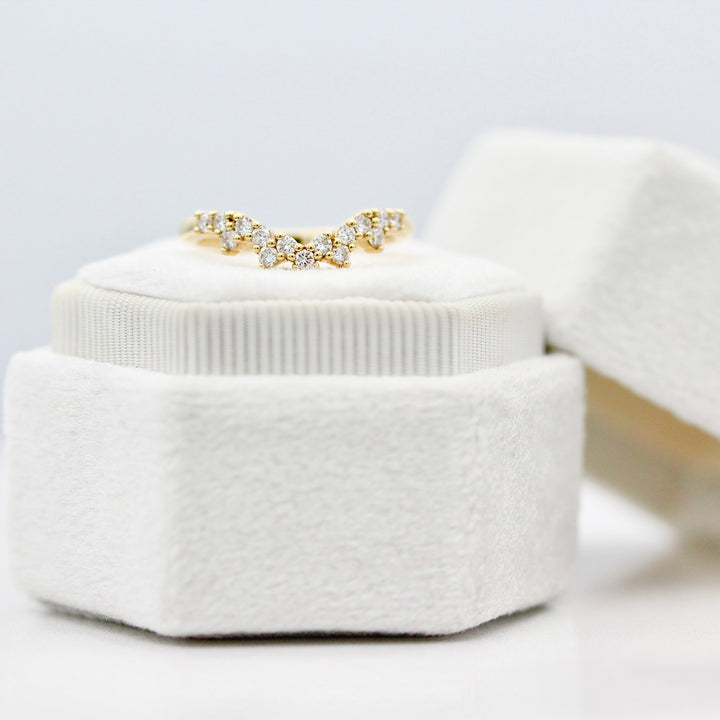 Yellow gold curved ring with round diamonds resting on a white velvet ring box