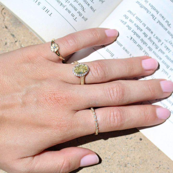 The Poppy flower pinky ring on a hand with a yellow diamond engagement ring and diamond wedding band all in yellow gold.