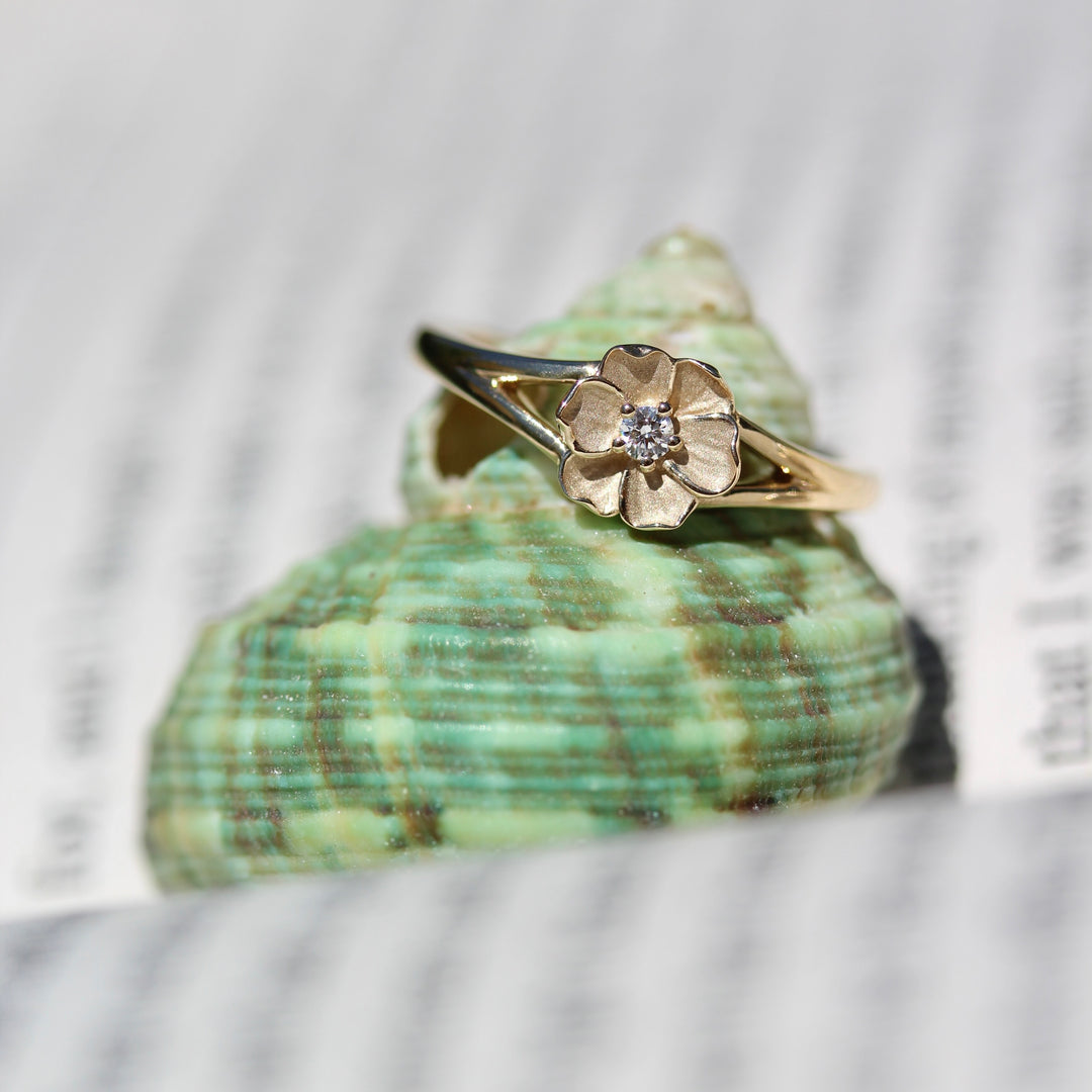 Yellow gold flower ring with round diamond center on a green shell against a blurred natural background