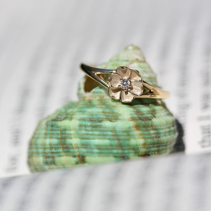 Yellow gold flower ring with round diamond center on a green shell against a blurred natural background