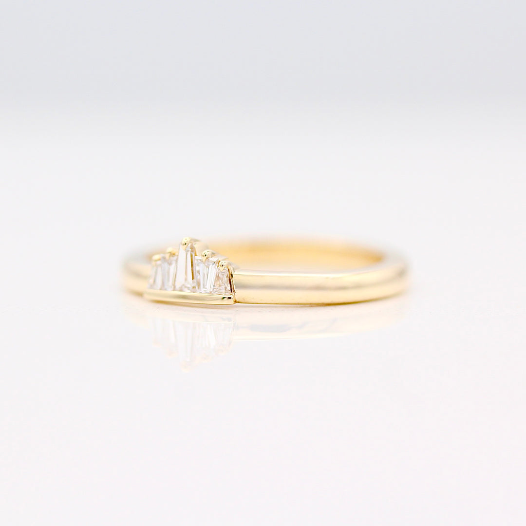 Yellow gold tapered diamond baguette ring with single claw prongs on a neutral background
