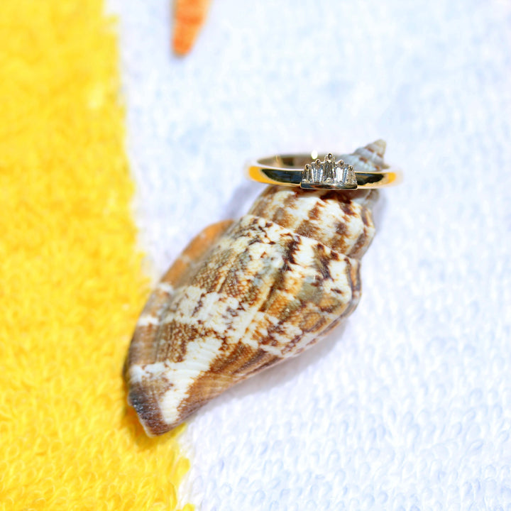 Yellow gold ring with a diamond baguettes on a seashell against a yellow and white background