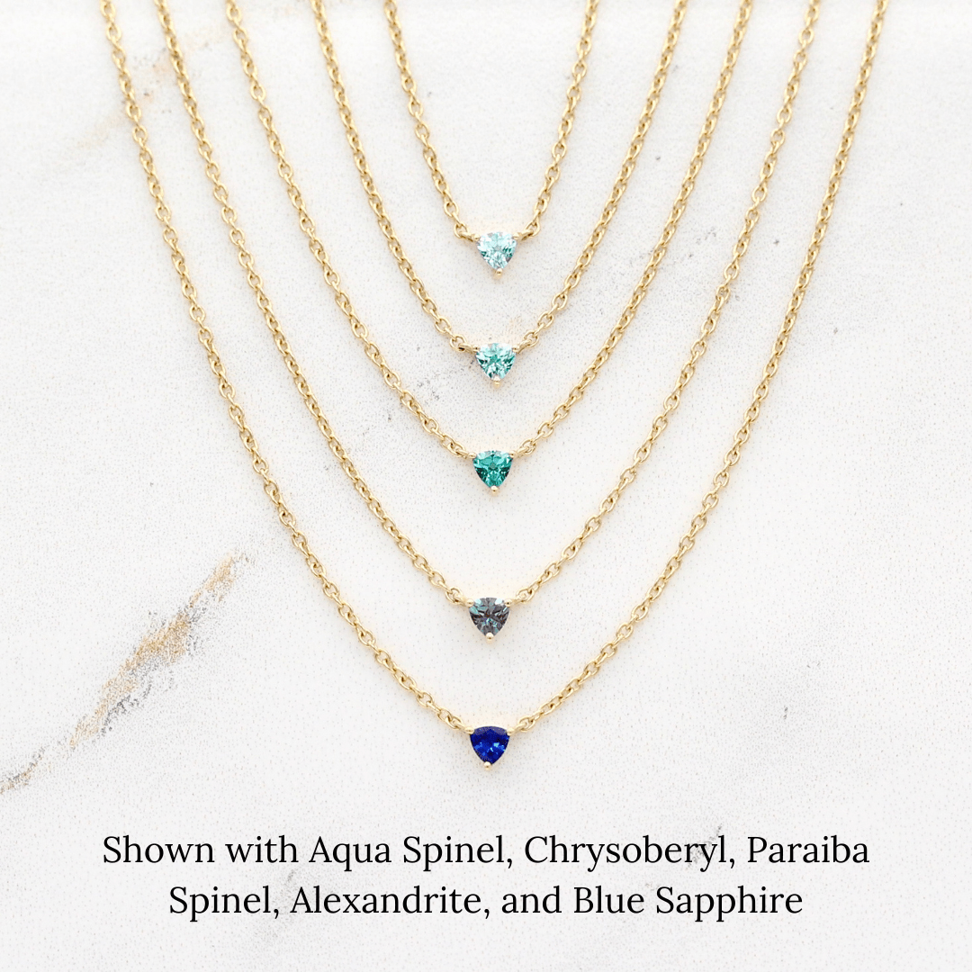 The March Tiny Trillion Birthstone Necklace with Aqua Spinel in Yellow Gold stacked with the August Tiny Trillion Birthstone Necklace with Chrysoberyl in Yellow Gold, the December Tiny Trillion Birthstone Necklace with Paraiba Spinel in Yellow Gold, and the June Tiny Trillion Birthstone Necklace with Alexandrite, and the September Tiny Trillion Birthstone Necklace with Blue Sapphire in Yellow Gold in Yellow Gold against a white background