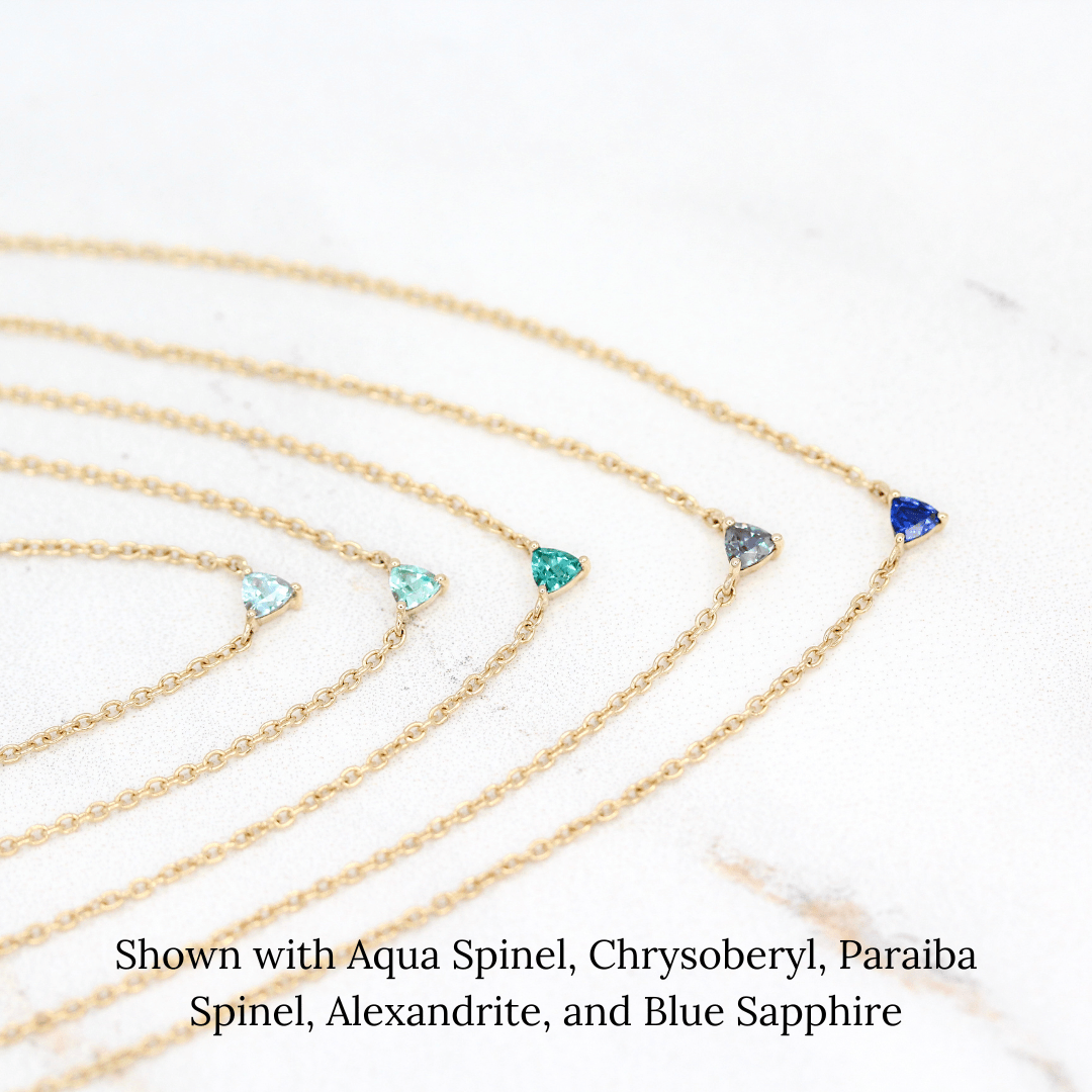 The March Tiny Trillion Birthstone Necklace with Aqua Spinel in Yellow Gold stacked with the August Tiny Trillion Birthstone Necklace with Chrysoberyl in Yellow Gold, the December Tiny Trillion Birthstone Necklace with Paraiba Spinel in Yellow Gold, and the June Tiny Trillion Birthstone Necklace with Alexandrite, and the September Tiny Trillion Birthstone Necklace with Blue Sapphire in Yellow Gold in Yellow Gold against a white background