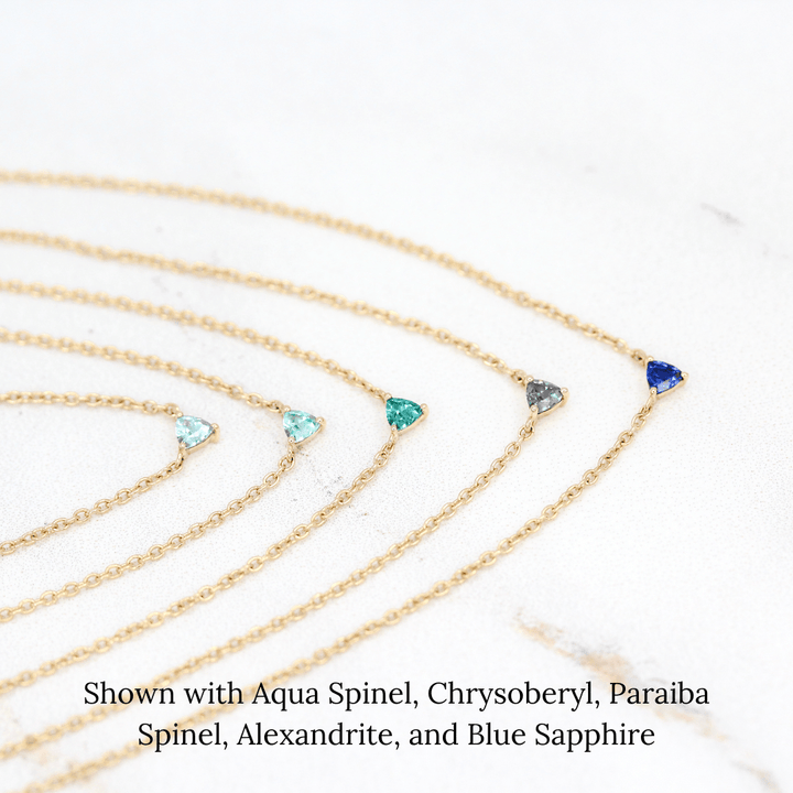 The March Tiny Trillion Birthstone Necklace with Aqua Spinel in Yellow Gold stacked with the August Tiny Trillion Birthstone Necklace with Chrysoberyl in Yellow Gold, the December Tiny Trillion Birthstone Necklace with Paraiba Spinel in Yellow Gold, and the June Tiny Trillion Birthstone Necklace with Alexandrite, and the September Tiny Trillion Birthstone Necklace with Blue Sapphire in Yellow Gold in Yellow Gold against a white background