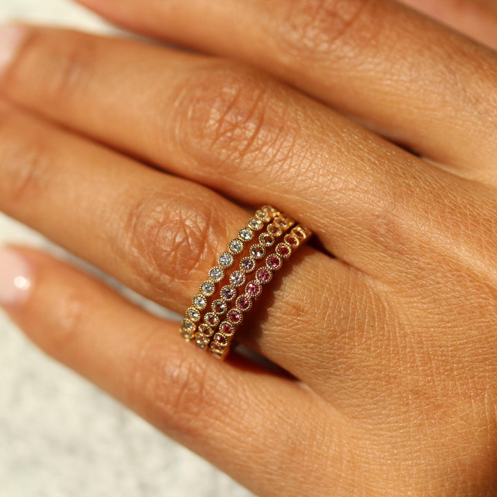 The April Florence Birthstone Band with Lab-Grown Diamond in Yellow Gold stacked with the June Florence Birthstone Band with Paraiba Spinel in Yellow Gold and the January Florence Birthstone Band with Padaparascha Sapphire in Yellow Gold modeled on a hand
