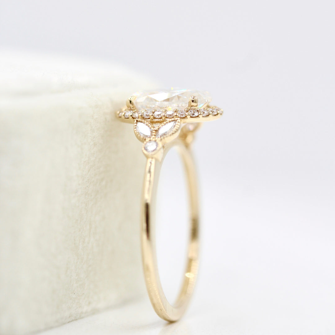 The Cate Ring (Oval) in yellow gold leaning against a white velvet ring box