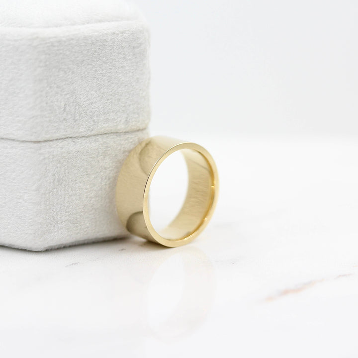 a gold wedding band leaning against a ring box