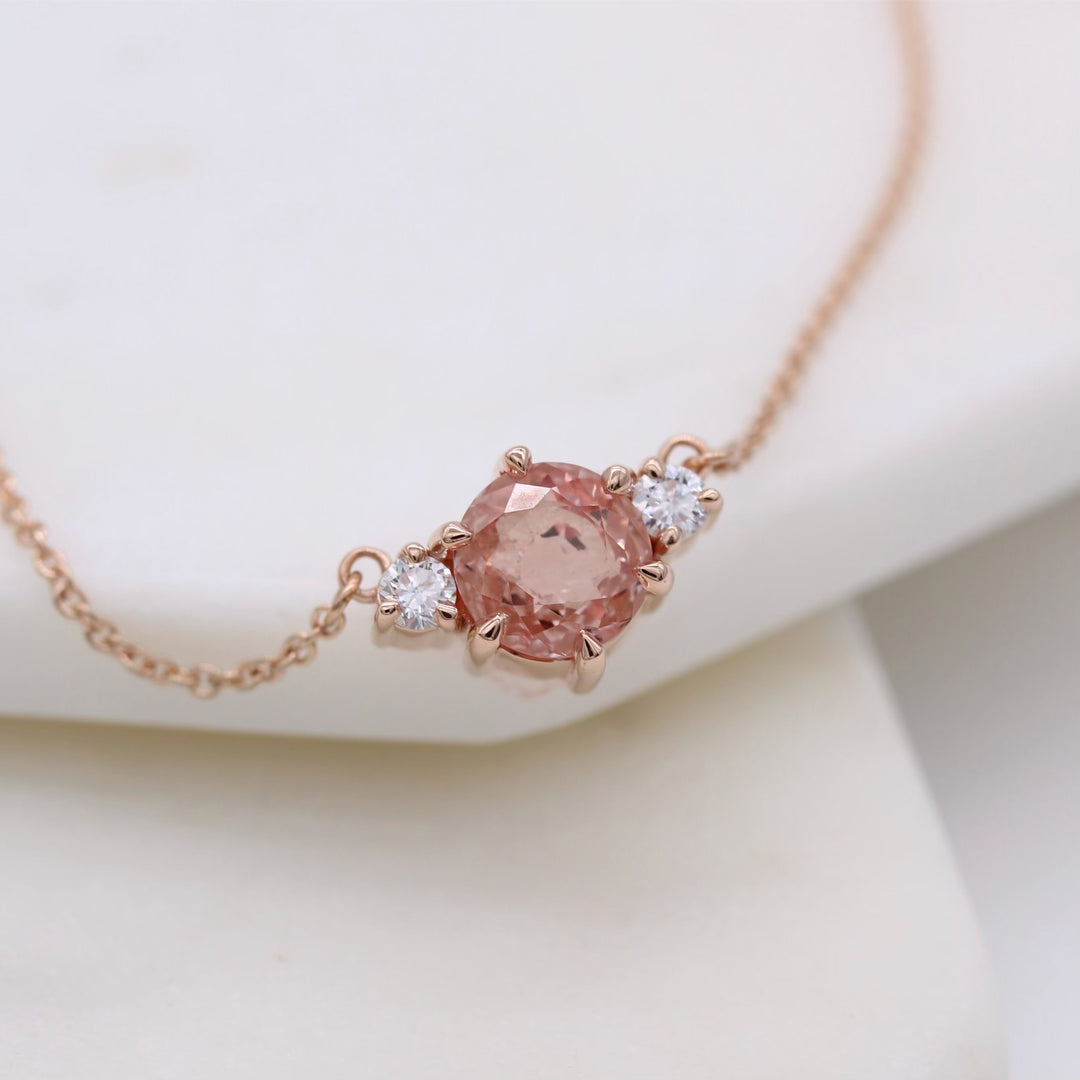 rose gold necklace with peachy-pink sapphire center and round diamond accents on a rose gold chain