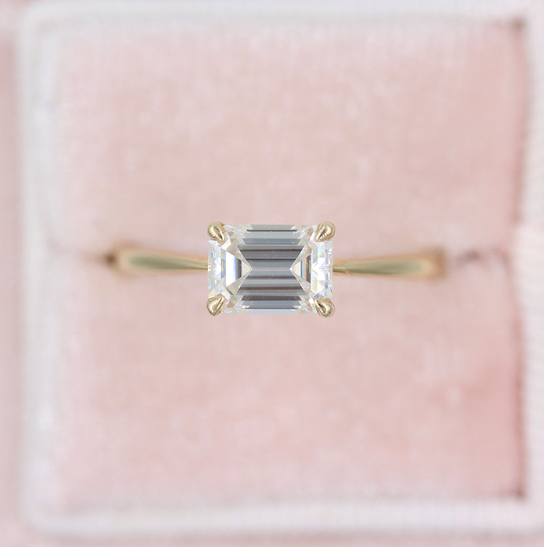 Emerald-cut diamond solitaire (east-west setting) in a light pink velvet ring box