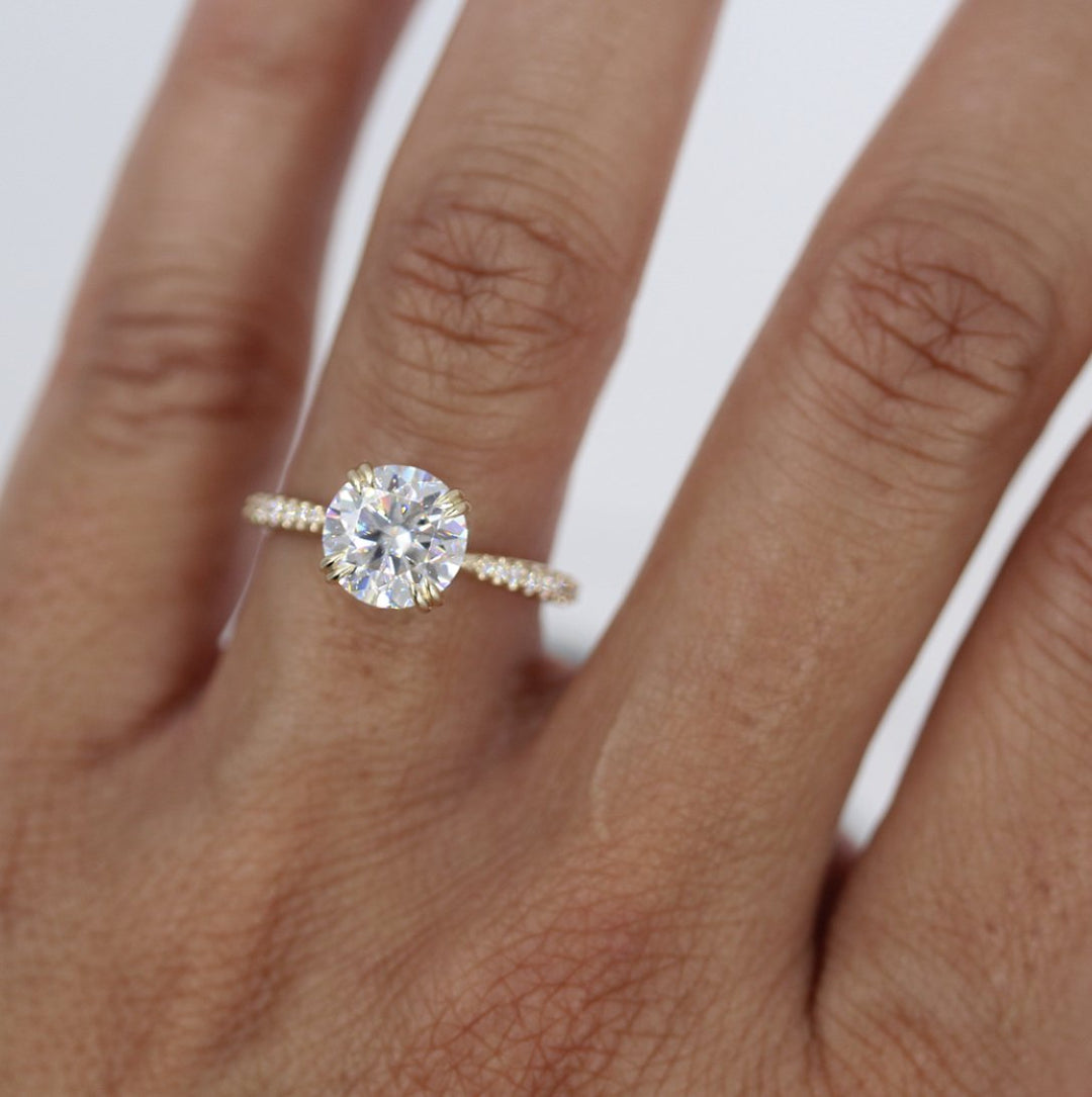 Hand wearing 2ct round engagement ring with double claw prongs and tapered pavé band