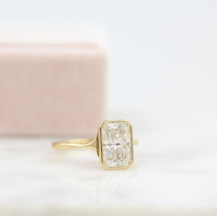 A gold radiant moissanite bezel engagement ring