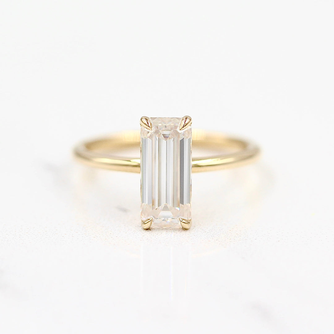 14k yellow gold elongated emerald solitaire engagement ring on a white background