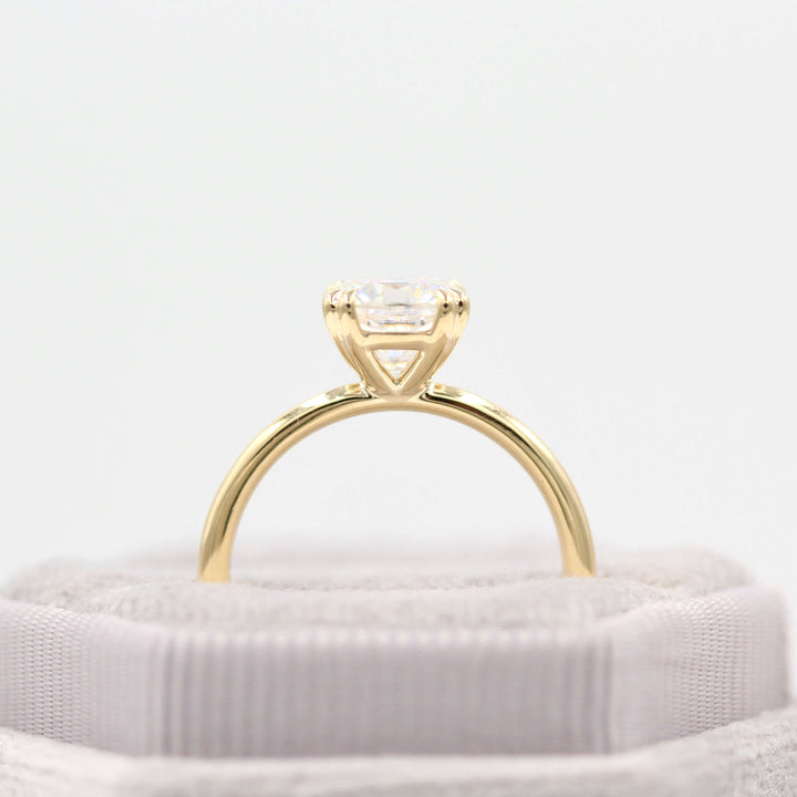 Grey velvet ring box holding 14k yellow gold solitaire cushion engagement ring