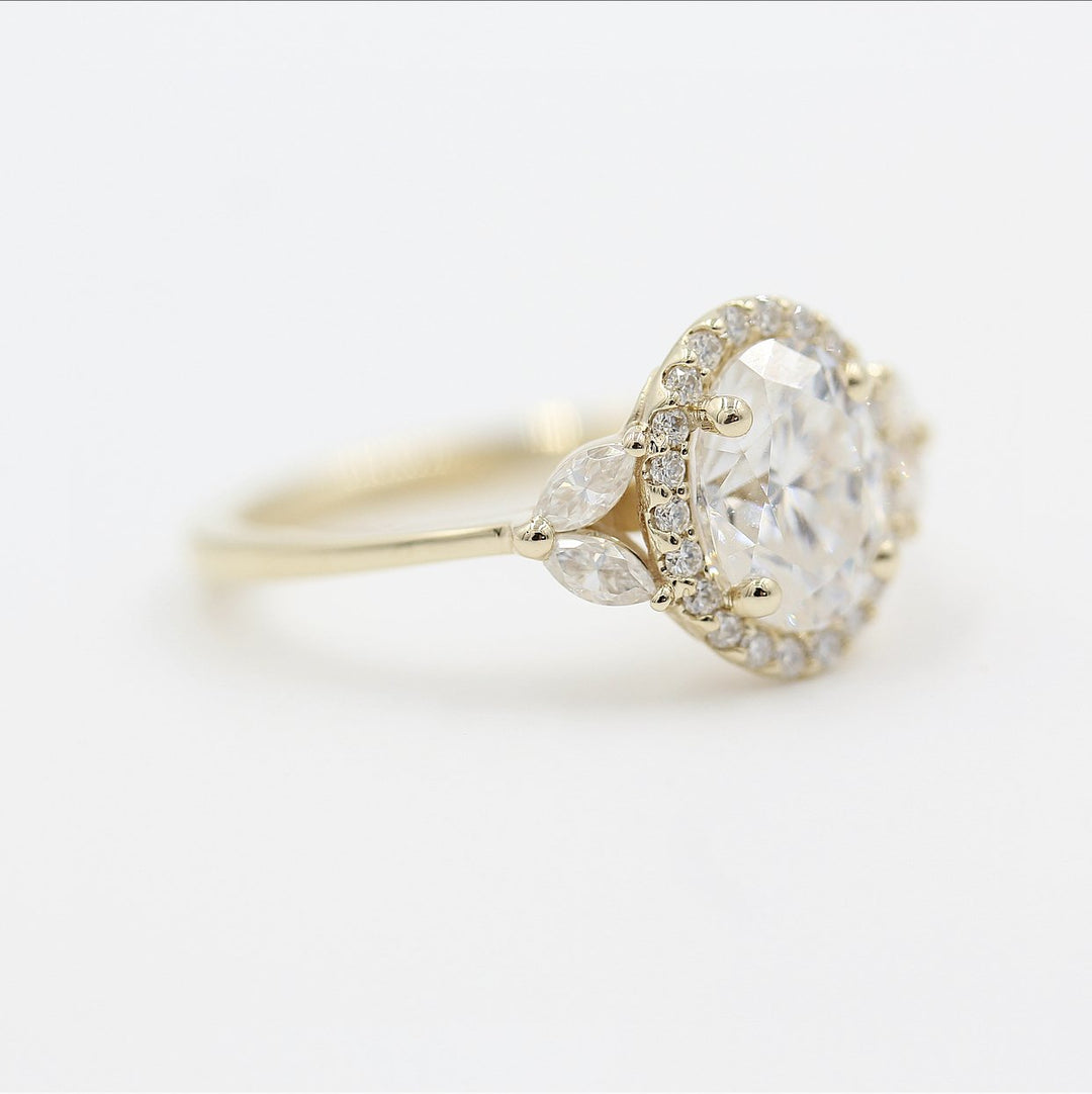 a yellow gold oval halo engagement ring on a white surface.