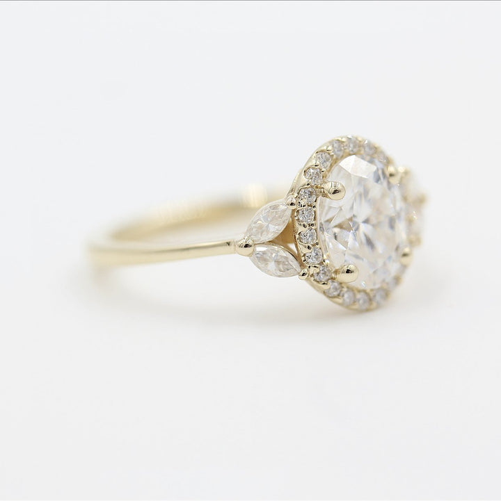 a yellow gold oval halo engagement ring on a white surface.